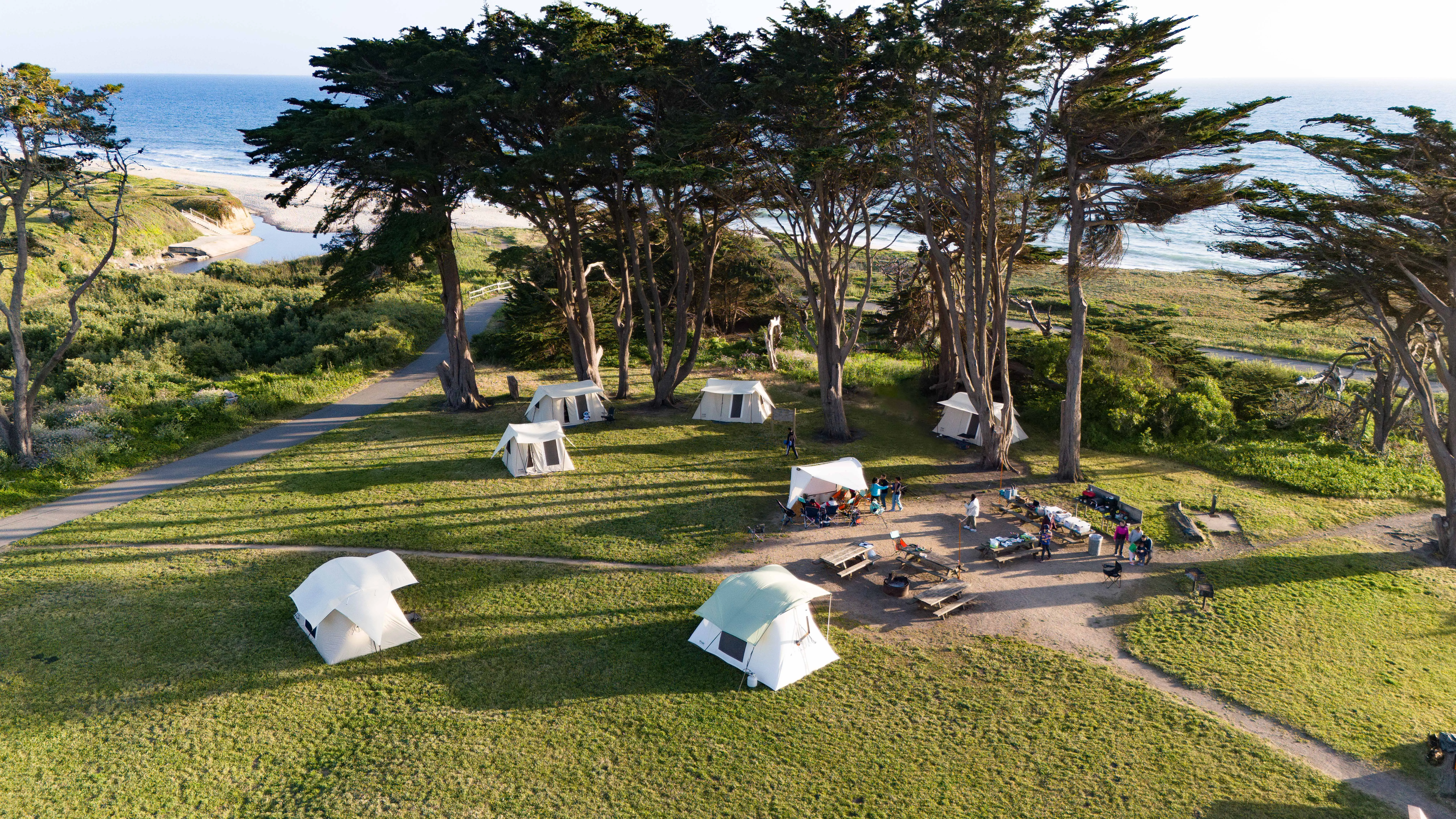 Aerial view of canvas tents pitched on a grassy bluff above the coast